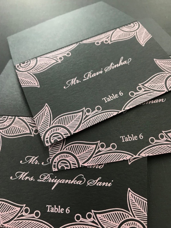 Escort cards in pink lace pattern on black with guest names and table numbers