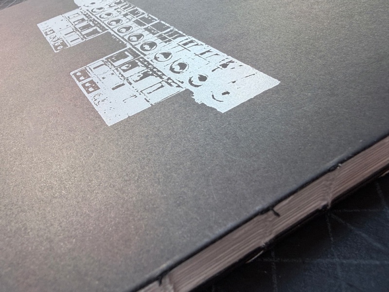 White ink pixel artwork on black book with exposed sewn spine